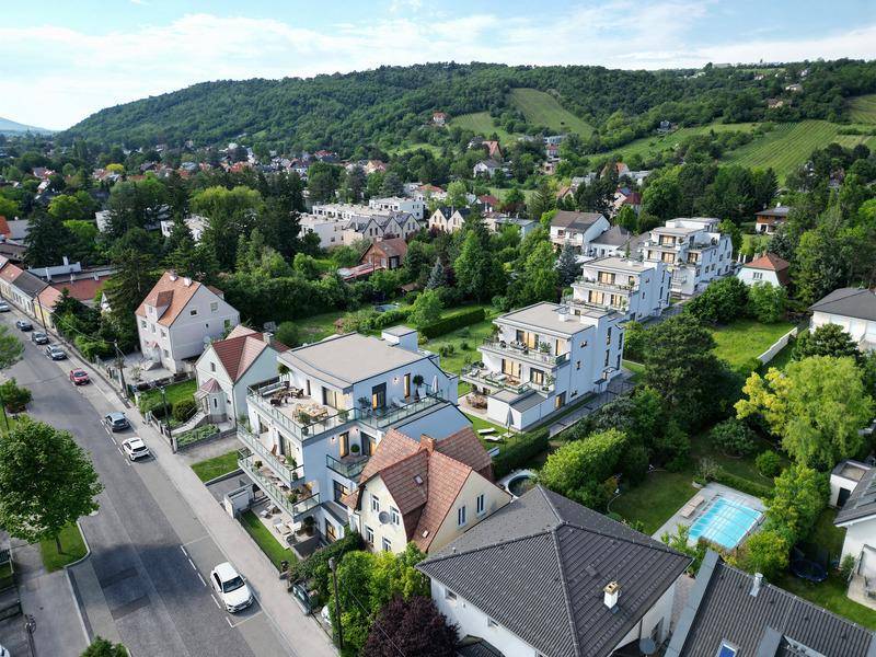 Luftaufnahme der modernen Wohngebäude eingebettet in eine grüne Hügellandschaft mit Weinbergen und Pool.