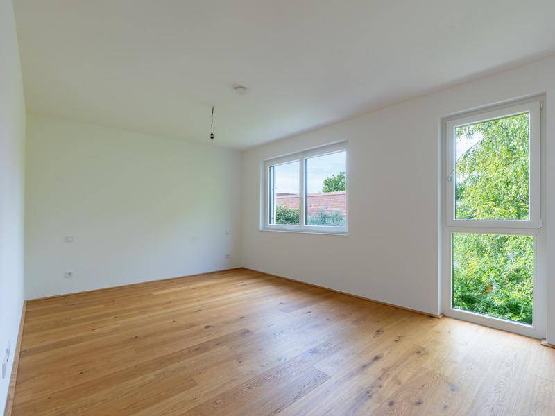 Helles Zimmer mit Holzboden und großem Fenster, das viel Tageslicht hereinlässt.