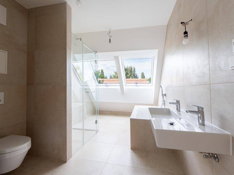 Modernes Badezimmer mit beigen Fliesen, Doppelwaschbecken, ebenerdiger Dusche und Dachfenstern.