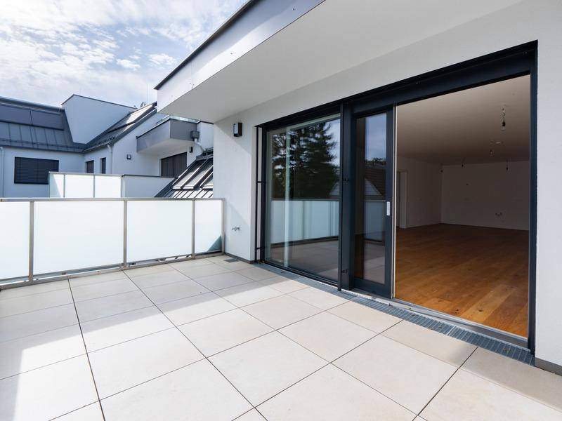 Geräumige Terrasse mit Fliesenboden und moderner Glasbrüstung, zugänglich vom Wohnbereich.