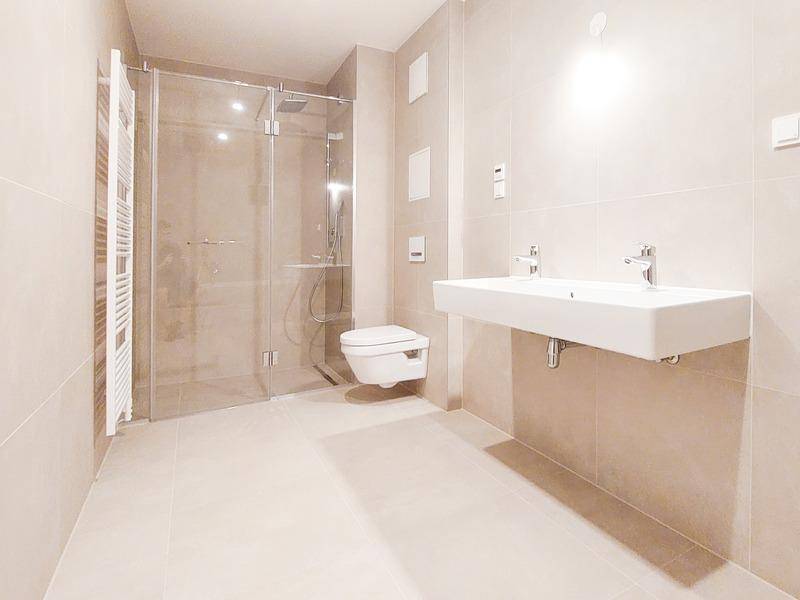 Modernes Badezimmer mit beigefarbenen Fliesen, Doppelwaschbecken, wandhängendem WC und ebenerdiger Dusche.
