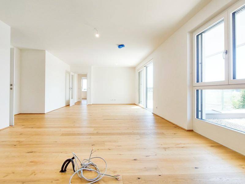 Heller, leerer Wohnbereich mit großen Fenstern und hochwertigem Holzparkettboden in einem Neubau.