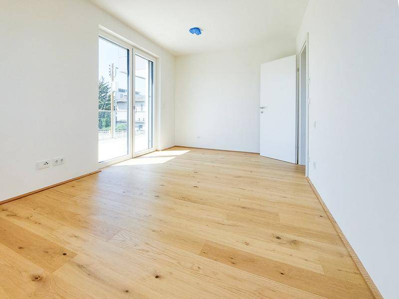 Lichtdurchflutetes Zimmer mit Holzboden und Zugang zu einem Balkon oder einer Terrasse.