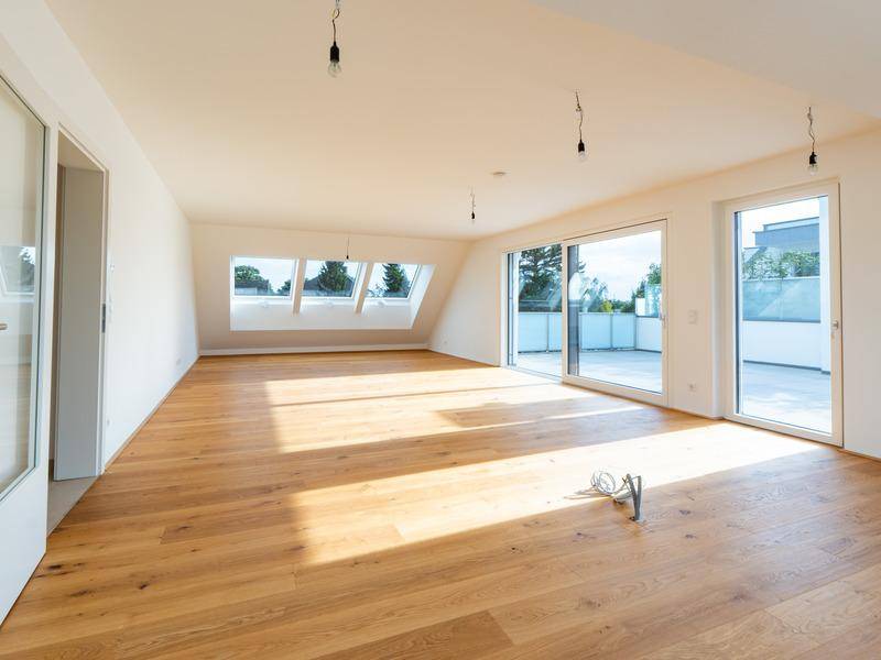 Großzügiger, lichtdurchfluteter Wohnbereich mit Holzboden, Dachschrägen und Zugang zur Terrasse.