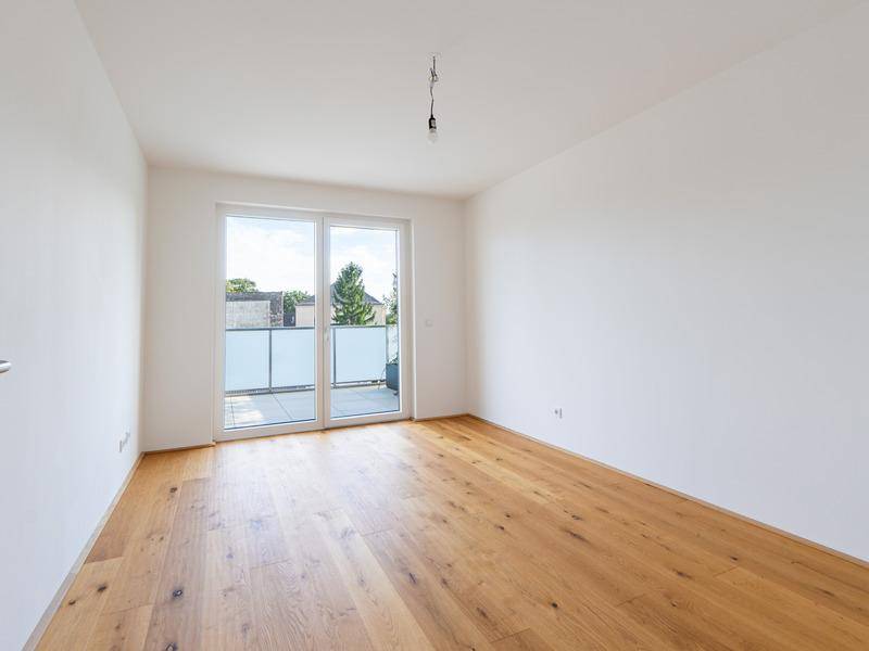 Helles Schlafzimmer mit Holzboden und Zugang zu einem französischen Balkon, bietet viel Tageslicht.