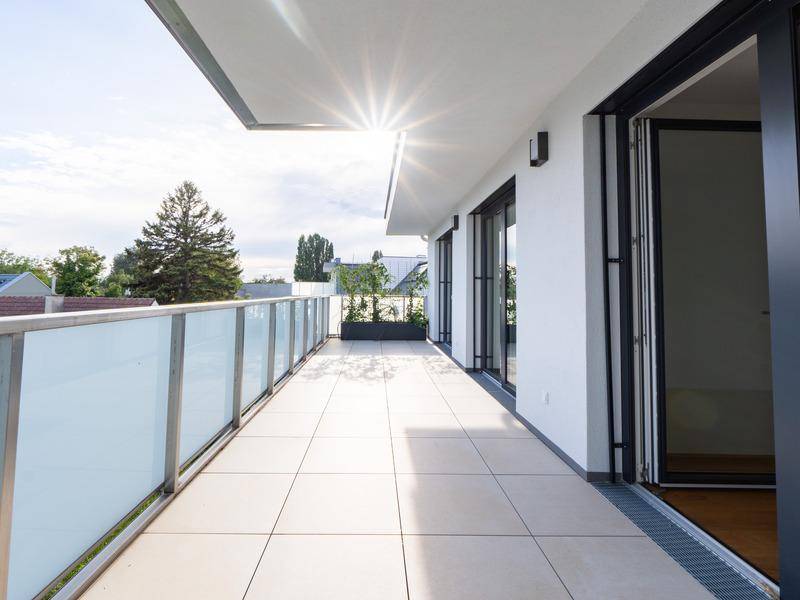 Langer Balkon mit Fliesenboden und Glasgeländer, bietet sonnige Stunden und Weitblick.