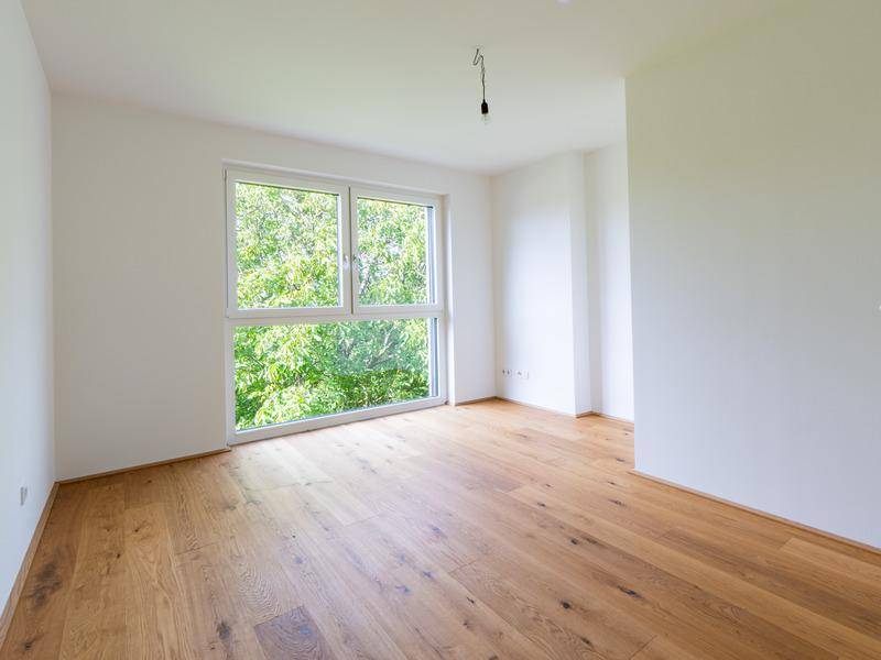 Lichtdurchflutetes Zimmer mit Holzboden und großem Fenster, das einen schönen Blick ins Grüne bietet.