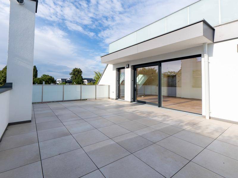 Geräumige Dachterrasse mit modernen Fliesen und Glasgeländer, ideal für Entspannung im Freien.