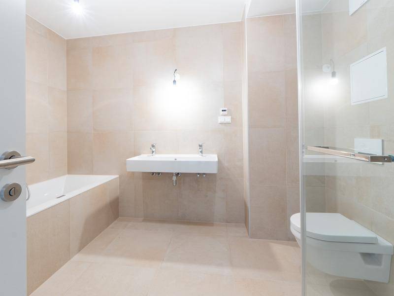 Modernes Badezimmer mit Doppelwaschbecken, Badewanne und begehbarer Dusche in hellen Beigetönen.