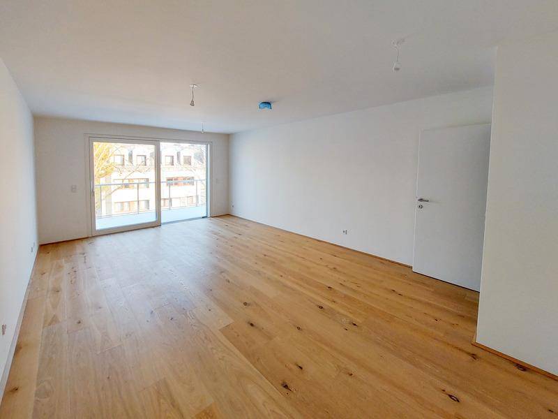 Heller, leerer Raum mit modernem Holzboden und Zugang zu einem Balkon.
