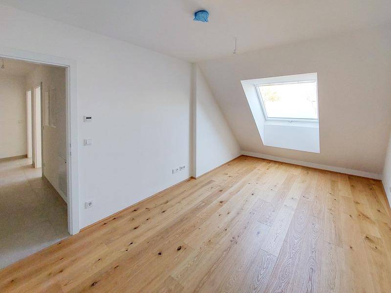 Helles Zimmer im Dachgeschoss mit Holzboden und schrägem Dachfenster.