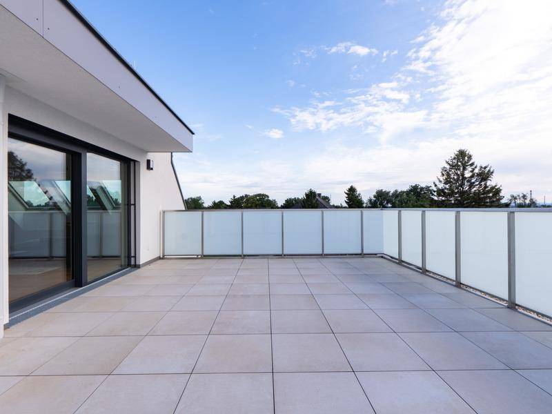 Große, geflieste Dachterrasse mit moderner Glasbrüstung und weitem Blick.