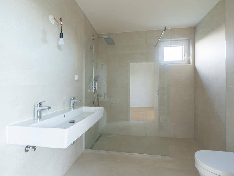 Modernes Badezimmer mit Doppelwaschbecken, ebenerdiger Dusche und hellen Fliesen.
