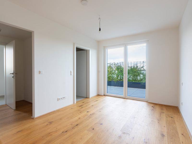 Heller Raum mit Holzboden und großen Fenstern, die Zugang zur Terrasse bieten.