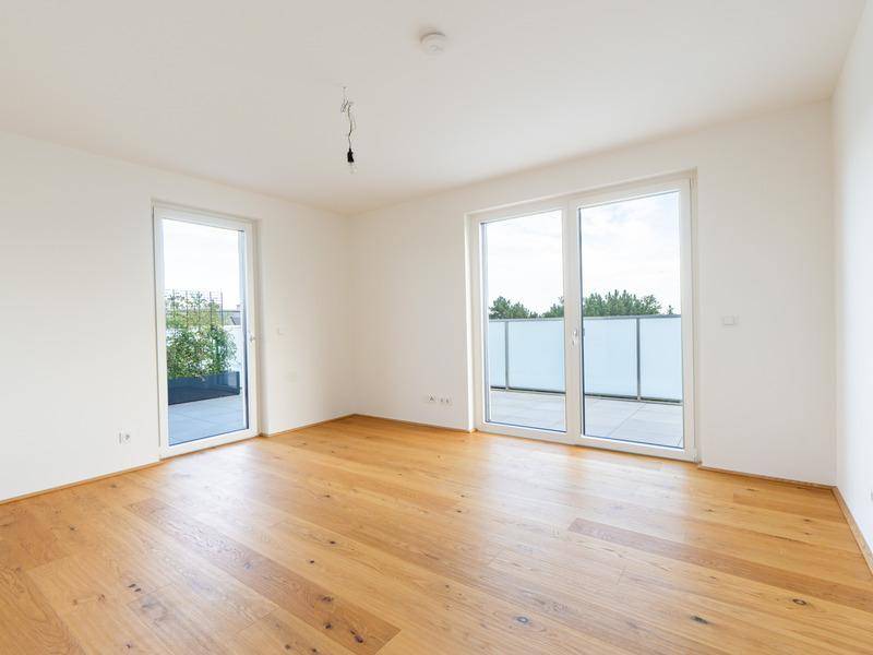 Lichtdurchfluteter Raum mit Holzboden und zwei Zugängen zu einer Außenterrasse.