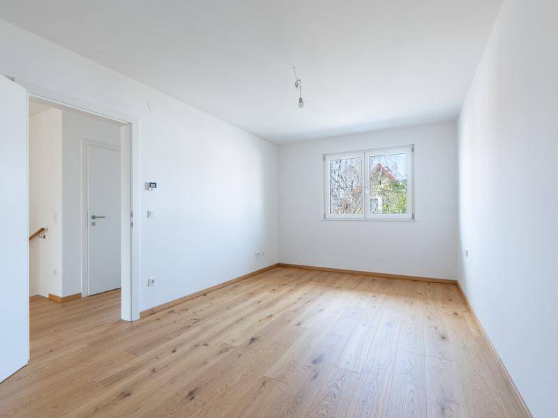 Helles Schlafzimmer mit Holzboden, weißen Wänden und einem Fenster mit Blick ins Grüne.
