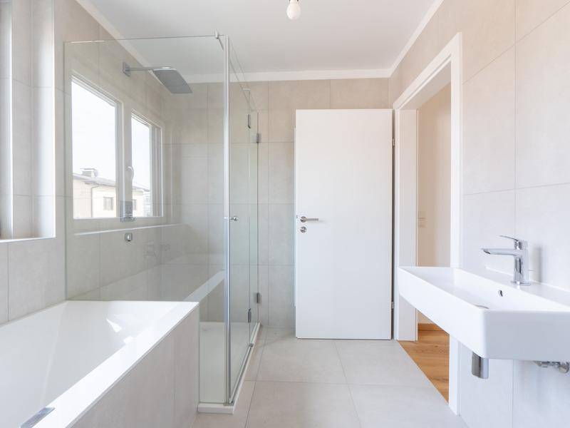 Modernes Badezimmer mit hellgrauen Fliesen, Badewanne, begehbarer Dusche und Fenster.