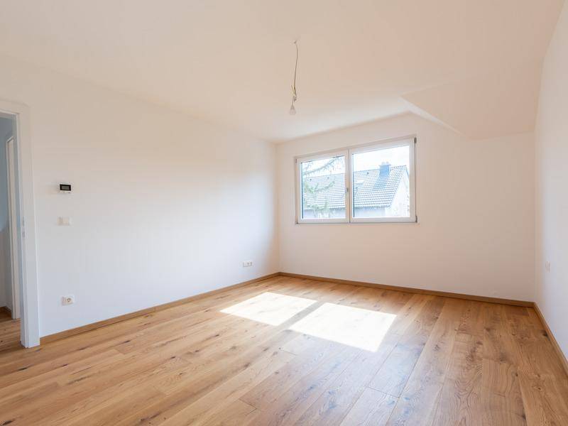 Helles Schlafzimmer mit Holzboden und einem Fenster mit Blick auf die Dächer.