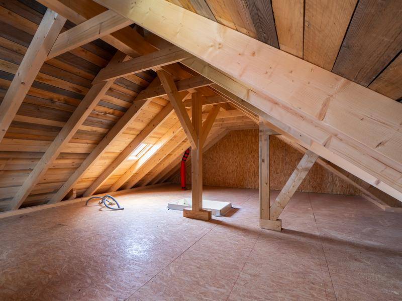 Unausgebauter Dachboden mit sichtbaren Holzbalken und Dachfenster.