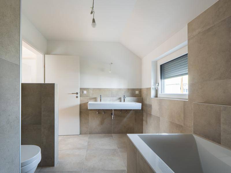 Modernes Badezimmer mit beigen Fliesen, Doppelwaschbecken und Badewanne.