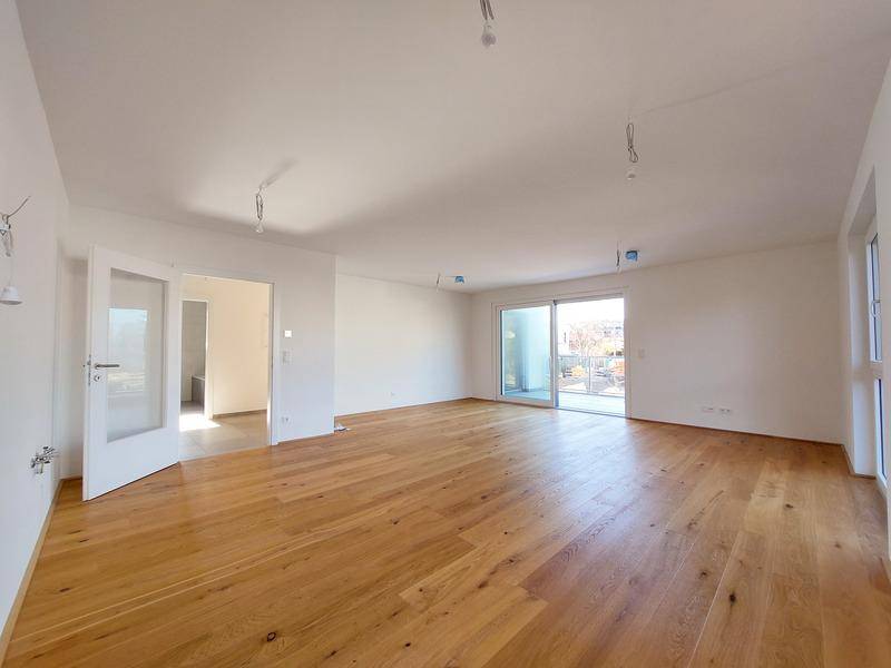 Heller, leerer Wohnraum mit Holzboden und Zugang zu einem Außenbereich.