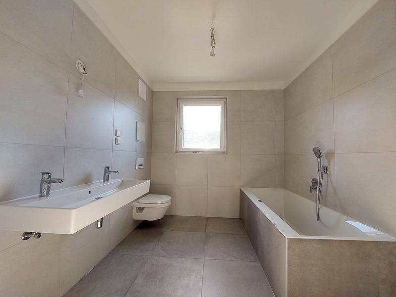Modernes Badezimmer mit hellgrauen Fliesen, Doppelwaschbecken und Badewanne.