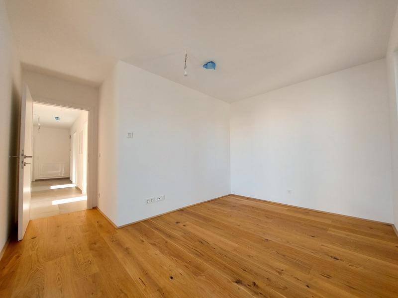Helles, leeres Zimmer mit Holzboden und weiß gestrichenen Wänden.