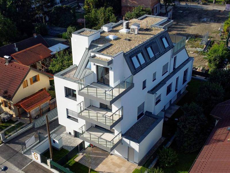 Luftaufnahme eines modernen Mehrfamilienhauses mit mehreren Balkonen und Flachdach.