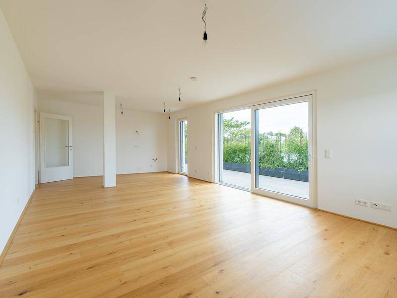 Heller, leerer Wohnraum mit Holzboden und großen Schiebetüren zur Terrasse.