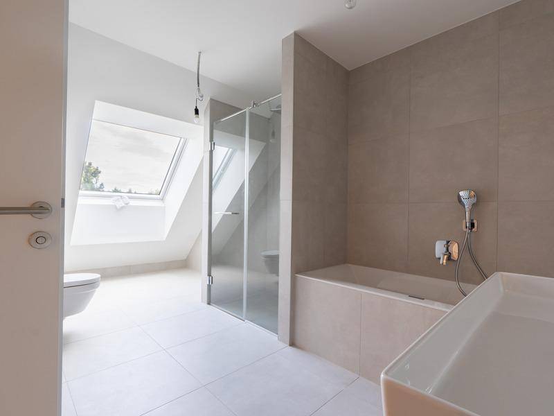 Modernes Badezimmer mit Badewanne, Dusche, WC und Dachfenster für Tageslicht.