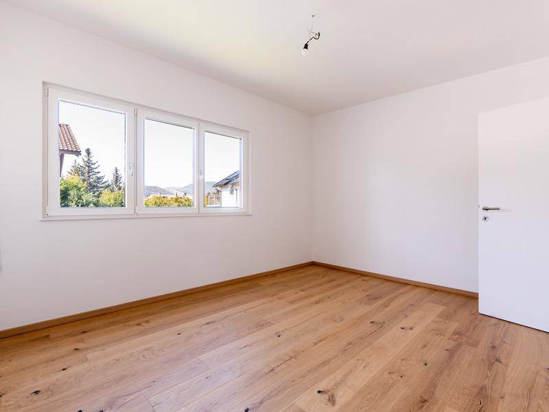 Leeres Schlafzimmer mit großen Fenstern und hellem Holzparkettboden, bietet viel Tageslicht.