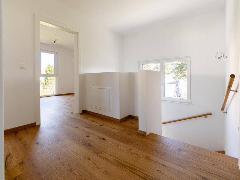 Heller Flur mit Holztreppe und Zugang zu weiteren Räumen im Obergeschoss, modern gestaltet.