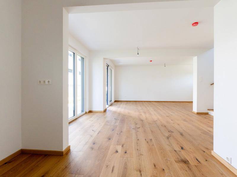 Helles, leeres Wohnzimmer mit großen Fenstern und neuem Holzparkettboden, bereit zur Einrichtung.