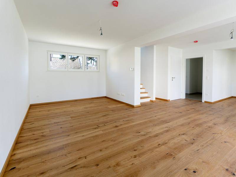 Geräumiges Wohnzimmer mit Holzboden und Blick ins Grüne durch die Fenster, ideal für Familien.