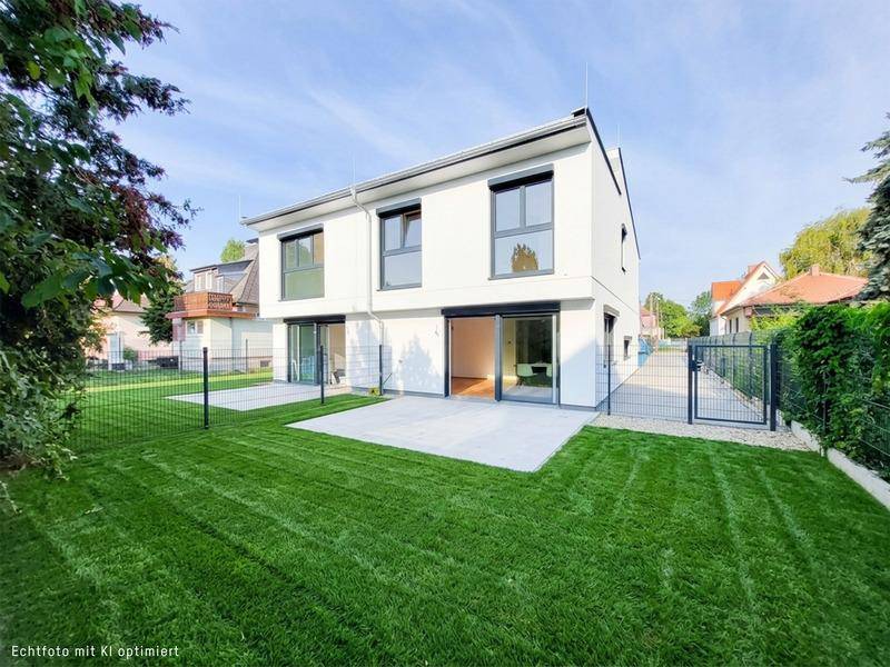 Neubau-Doppelhaushälfte mit gepflegtem Rasen, Terrasse und moderner Architektur.