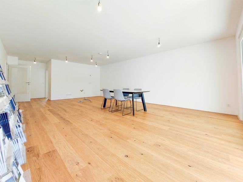 Helles, offenes Zimmer mit Holzboden und viel Tageslicht, ideal als Wohn- oder Essbereich.