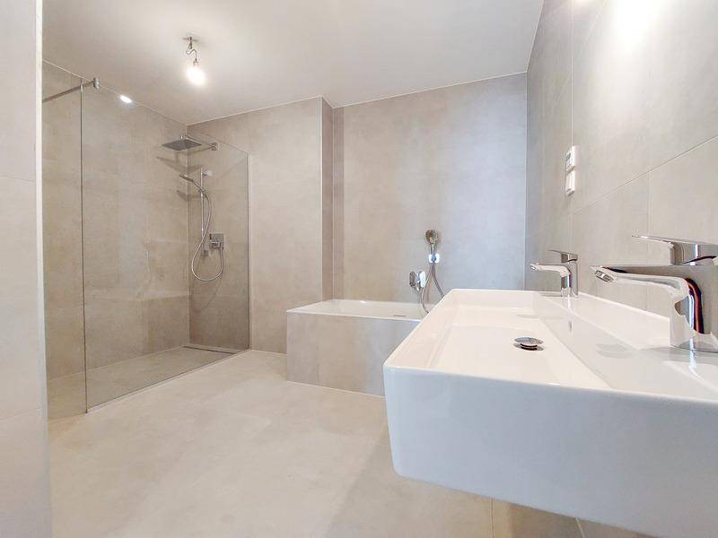 Modernes Badezimmer mit Doppelwaschbecken, großer begehbarer Dusche und Badewanne in hellen Fliesen.