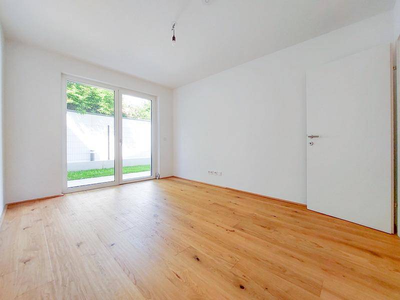 Helles Schlafzimmer mit Holzboden und direktem Zugang zum Gartenbereich durch große Terrassentüren.