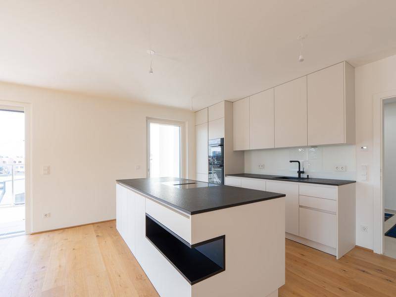 Moderne Einbauküche mit Kochinsel, schwarzen Arbeitsplatten und integrierten Geräten in hellem Raum.
