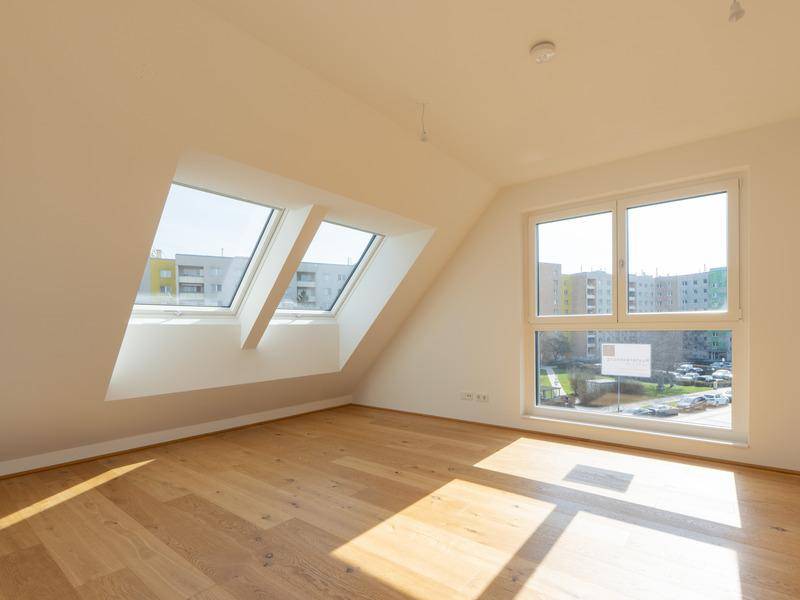 Helles Zimmer im Dachgeschoss mit schrägen Wänden, Dachfenstern und Holzboden.