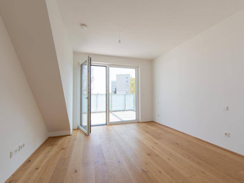 Lichtdurchflutetes Zimmer mit Holzboden und Zugang zu einem Balkon oder einer Terrasse.