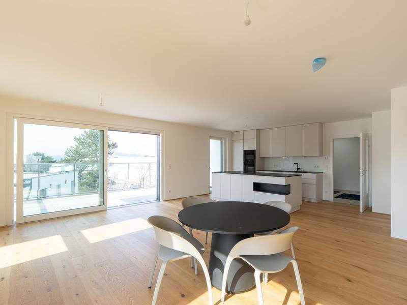 Heller offener Wohn-Essbereich mit moderner Küche, Holzboden und Zugang zu einer großen Terrasse.