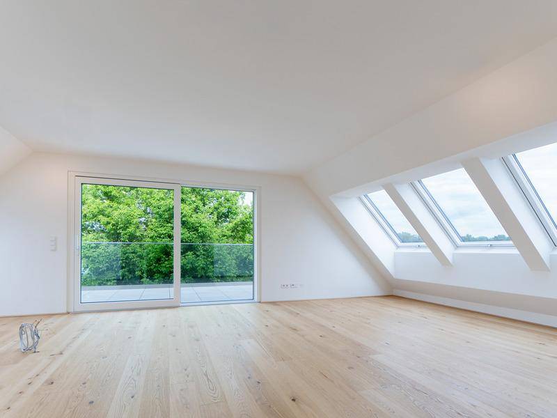 Lichtdurchfluteter Raum mit Holzboden, Schiebetüren und mehreren Dachfenstern.