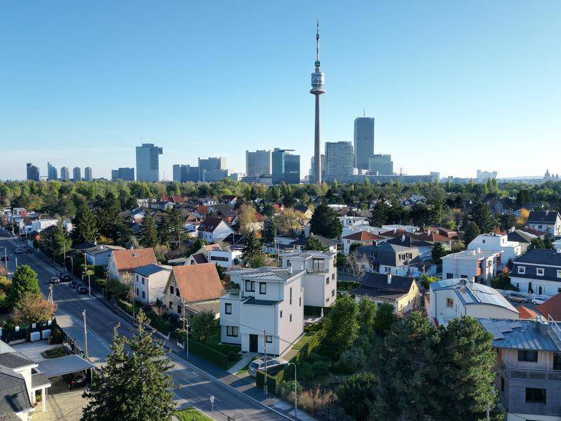 Luftaufnahme eines modernen Hauses in einer grünen Wohngegend mit Stadtblick und Donauturm.