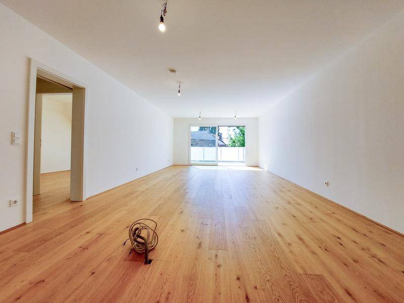 Helles, leeres Zimmer mit Holzboden und Zugang zu einem Balkon, ideal als Wohnbereich nutzbar.
