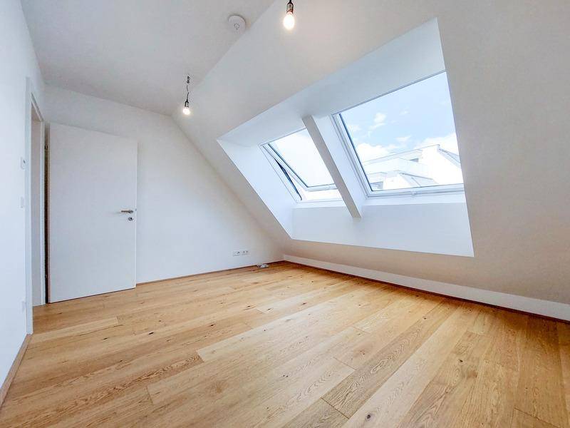 Helles Dachzimmer mit schrägen Wänden, Holzboden und großen Dachfenstern für viel Tageslicht.