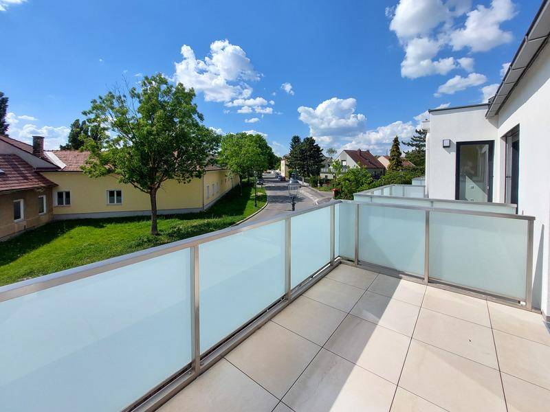 Geräumiger Balkon mit Glasgeländer und Fliesenboden, bietet einen Blick auf die grüne Umgebung.