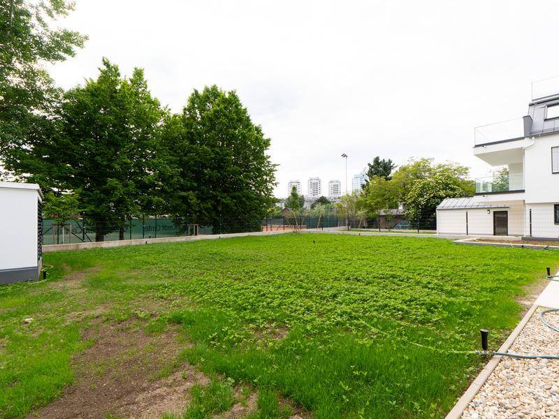 Große Rasenfläche mit Bäumen und einem Tennisplatz im Hintergrund, ideal für Freizeitaktivitäten.
