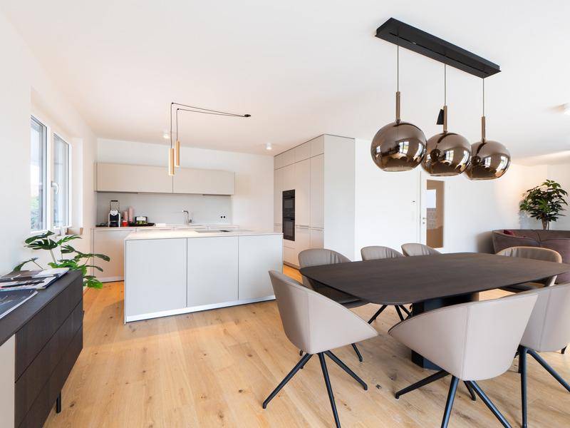 Moderne offene Küche mit Kücheninsel, integrierten Geräten und Essbereich mit stilvollen Pendelleuchten.