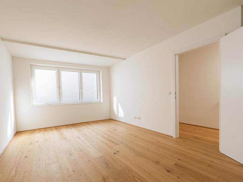 Helles Schlafzimmer mit Holzboden und großen Fenstern, bereit zur individuellen Gestaltung.